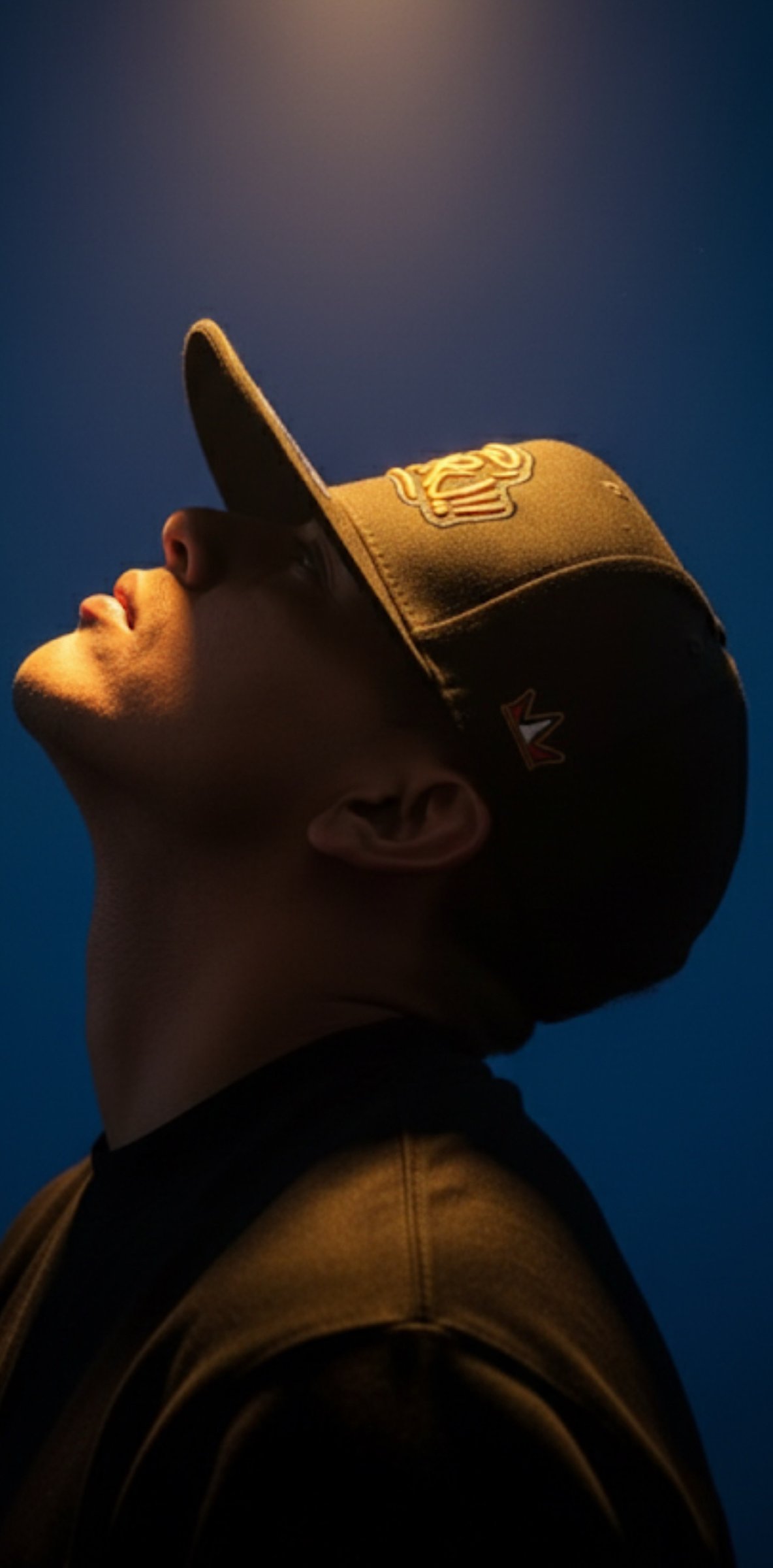 Profile portrait of a model looking up in a black snapback, lit in blue and amber