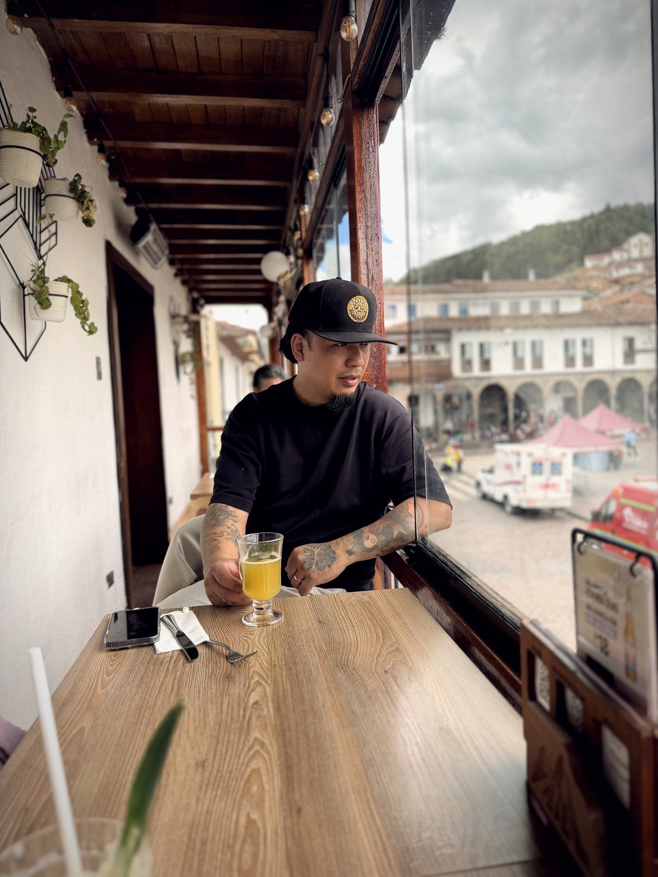 NG, fundador de Peru Street, con la gorra del sol Inti en un balcón frente a una plaza peruana